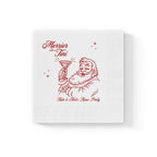 Close-up of Merrier with a Tini Christmas napkin showing the festive red Santa illustration holding a martini glass and elegant script lettering.