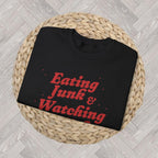 Folded funny retro Christmas sweatshirt displayed in a cosy holiday setting, designed for eating snacks and watching Christmas films.