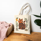 Woman carrying a Mediterranean Matisse cat tote bag featuring olive leaves, citrus fruit, and terracotta-inspired artwork.