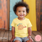 Smiling toddler wearing butter yellow personalized pizza birthday shirt with ‘Amelia is One’ design, custom Italian theme first birthday outfit for baby girl or boy.