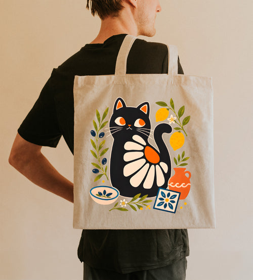 Mediterranean black cat tote bag featuring olive branches, lemons, terracotta pottery, and decorative tile artwork on natural cotton canvas.