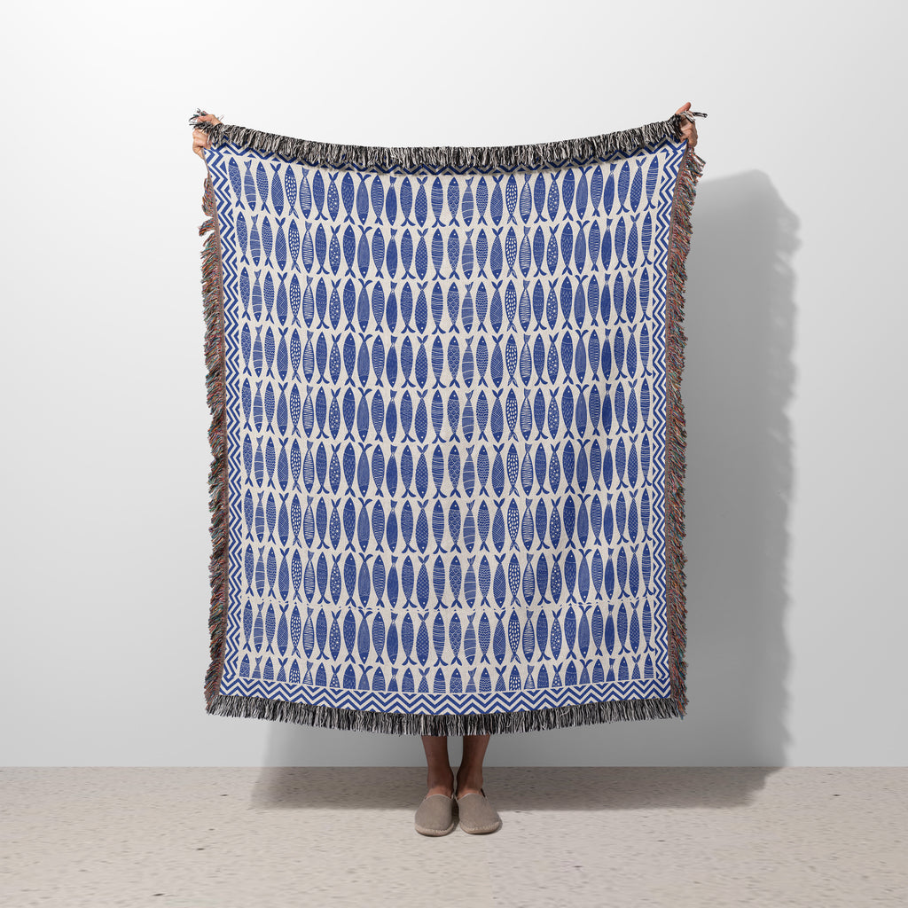 Blue Fish woven blanket featuring a repeating ocean fish pattern in blue and ivory with colorful fringed edges
