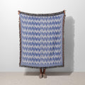 Blue Fish woven blanket featuring a repeating ocean fish pattern in blue and ivory with colorful fringed edges