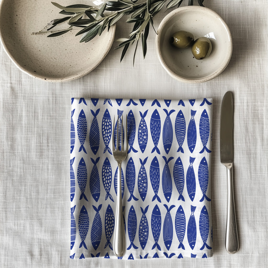 Single blue fish dinner napkin folded on table showcasing one-sided ocean pattern print and premium reusable cotton fabric