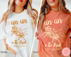 Ivory Cin Cin the Bride shirt lifestyle shot – cozy styling with soft cardigan and iced beverage, highlighting bridal party DTG tee for fun weekend wear.
