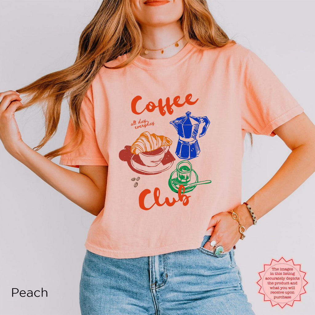 Peach coffee club cropped tee with retro illustrations of coffee and croissant, bringing style to your coffee-loving wardrobe.