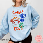 Light blue Coffee Club sweatshirt with colorful graphic design, featuring a croissant, coffee cup, and espresso machine. Ideal for coffee enthusiasts.