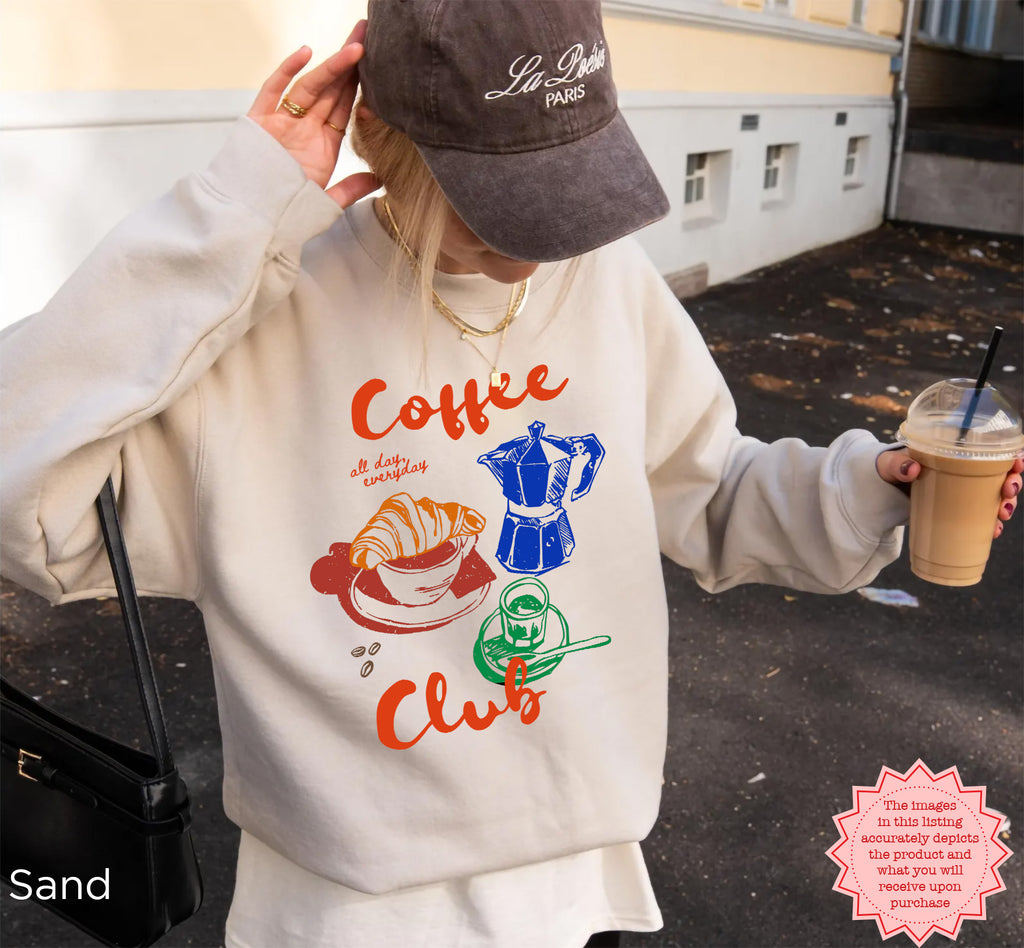 Sand-colored Coffee Club sweatshirt with a cozy, retro coffee graphic of a croissant, coffee cup, and espresso machine. A must-have for coffee lovers.