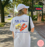 Cote d’Azur coastal graphic t-shirt in ash, featuring watercolor oysters, lemons, and lobster design, worn outdoors on a sunny street, perfect for summer beach style and lobster roll lovers.