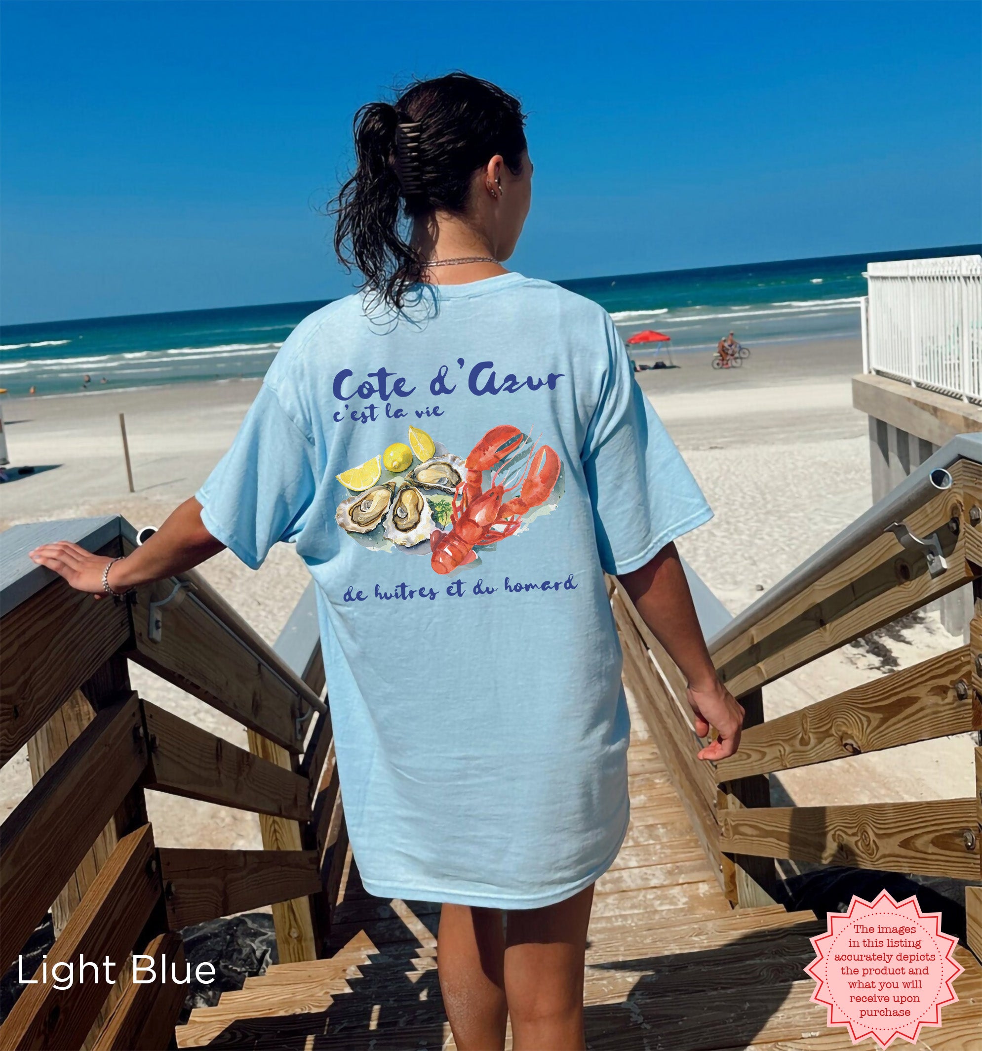 Light blue Cote d’Azur summer vacation t-shirt with coastal watercolor lobster and oyster graphic, worn at the beach, ideal for seafood enthusiasts and French Riviera lovers.