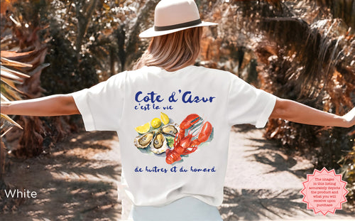 White Cote d’Azur t-shirt with watercolor lobster, oysters, and lemons design, worn outdoors with arms outstretched, coastal vacation style and ideal gift for seafood and lobster lovers.
