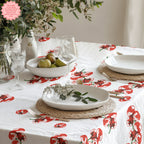 Tomato Block Print Tablecloth featuring a vibrant red tomato design, displayed on a rustic dining table with neutral plates and wine glasses. A fresh, Mediterranean-inspired setting perfect for casual dining.