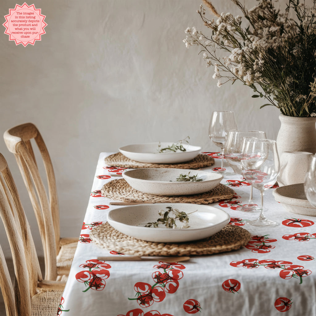 Tomato Block Print Tablecloth in a playful red and white design, featuring a fresh tomato pattern, displayed on a clean dining table with neutral plates and a flower arrangement. Perfect for Mediterranean-inspired decor.