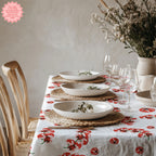 Tomato Block Print Tablecloth in a playful red and white design, featuring a fresh tomato pattern, displayed on a clean dining table with neutral plates and a flower arrangement. Perfect for Mediterranean-inspired decor.