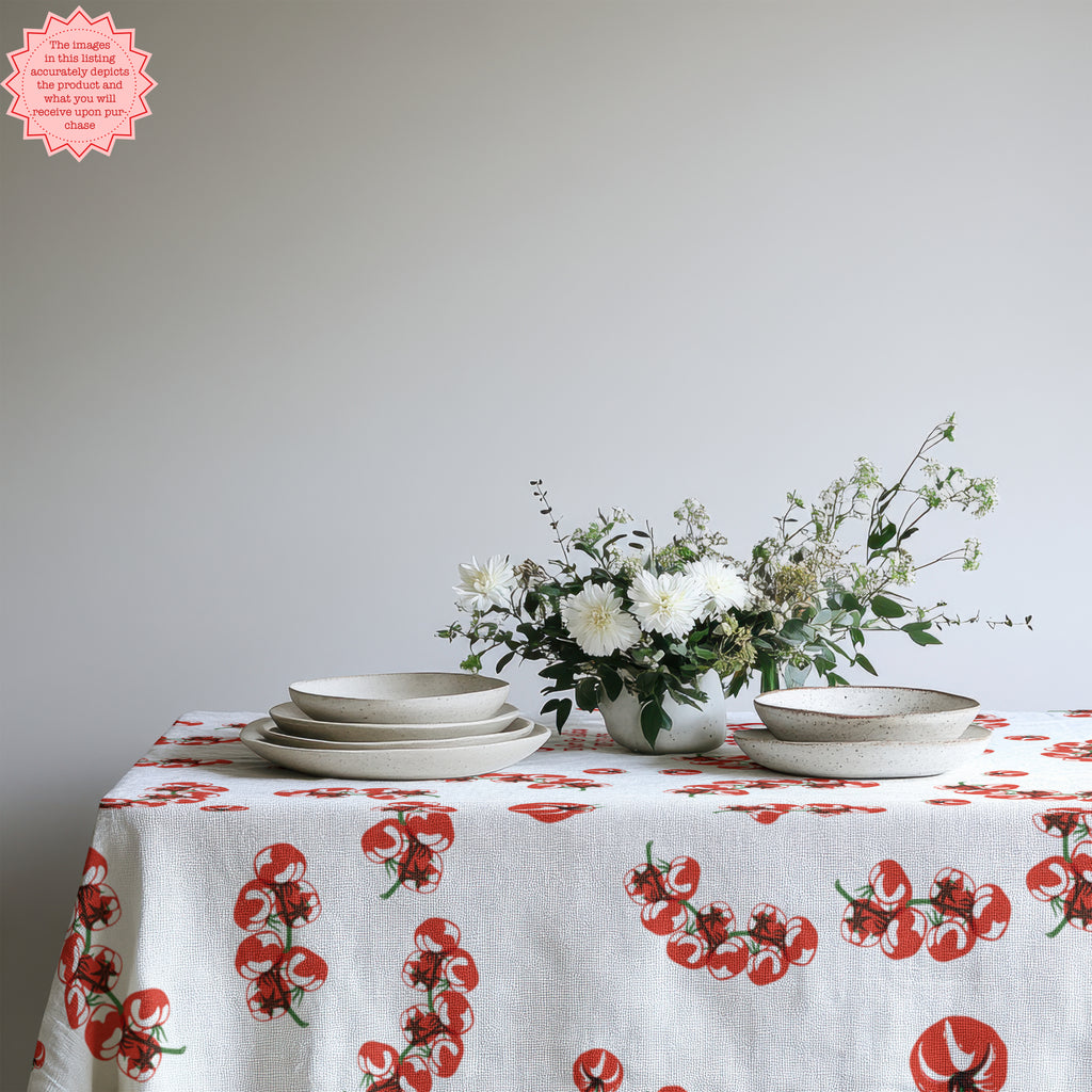Mediterranean Tomato Block Print Tablecloth with vibrant tomato illustrations, styled on a rustic dining table with neutral dinnerware, glasses, and a simple vase of flowers for a fresh and welcoming dining look.