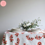 Mediterranean Tomato Block Print Tablecloth with vibrant tomato illustrations, styled on a rustic dining table with neutral dinnerware, glasses, and a simple vase of flowers for a fresh and welcoming dining look.