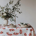 Fresh and colorful Mediterranean-inspired Tomato Block Print Tablecloth on a dining table with a bowl of apples, wine glasses, and delicate greenery. The playful tomato design brings bold style to the table setting.