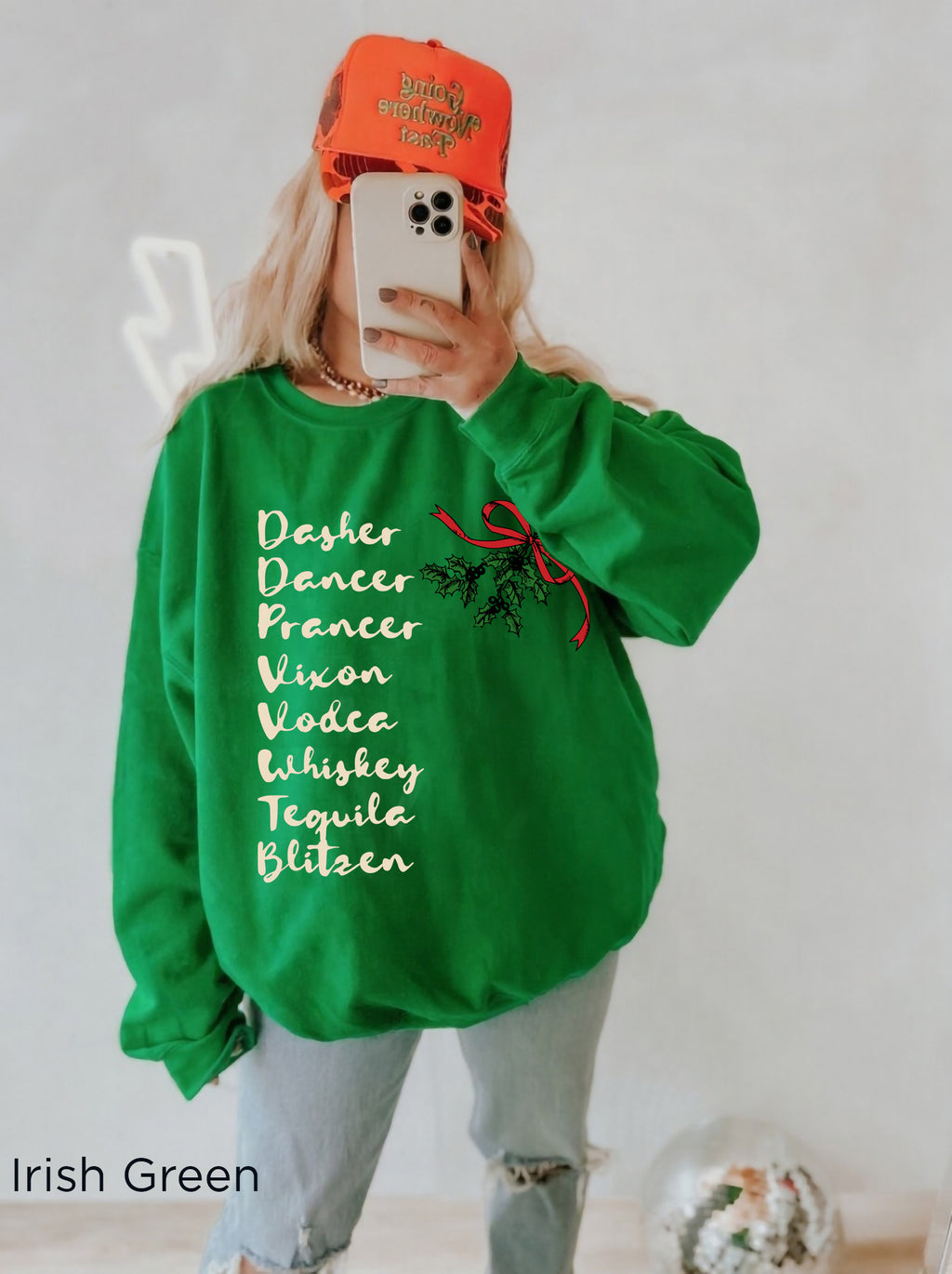 Woman wearing a funny Christmas cocktail sweatshirt with festive lettering, styled with light denim shorts in a cosy holiday setting.