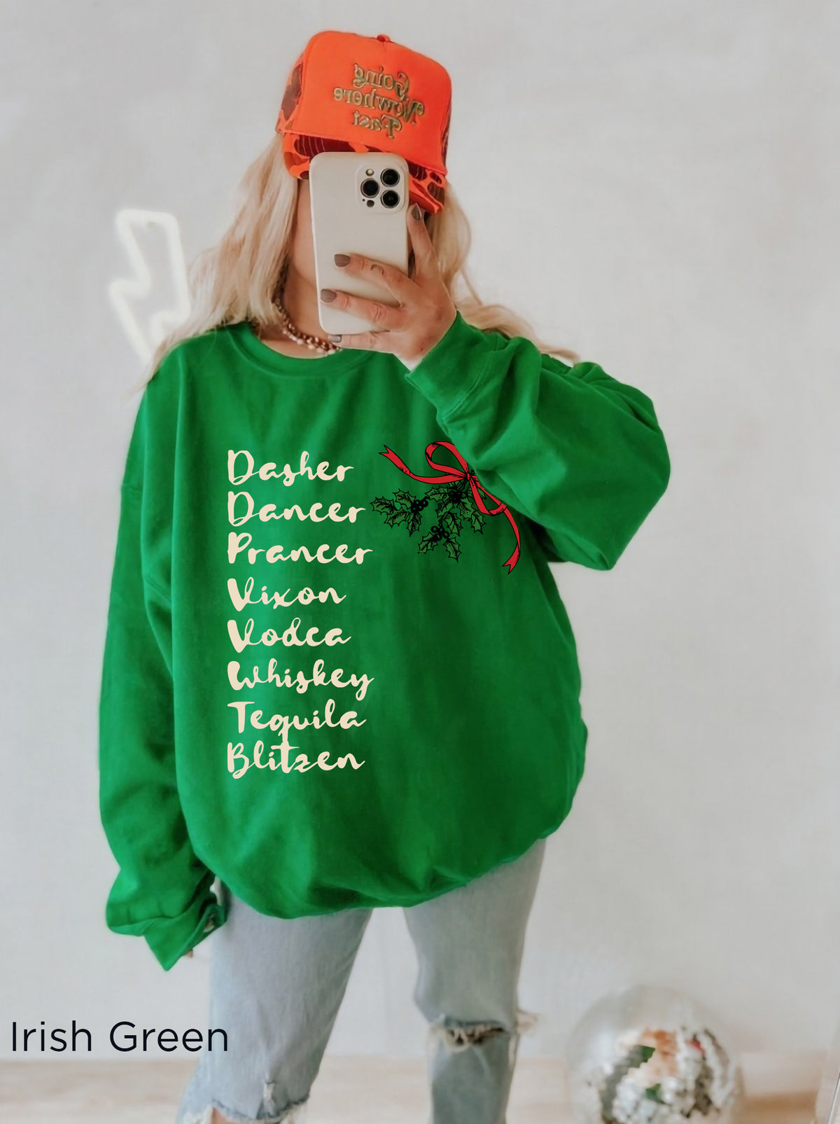 Woman wearing a funny Christmas cocktail sweatshirt with festive lettering, styled with light denim shorts in a cosy holiday setting.