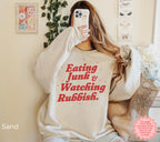 Close-up of a funny Christmas crewneck sweatshirt featuring retro-inspired “Eating Junk & Watching Rubbish” lettering.