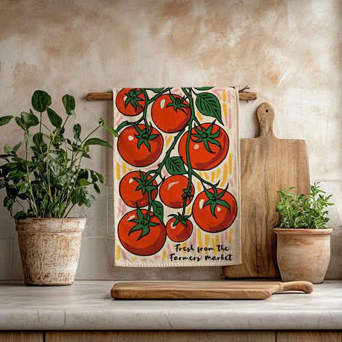Colorful cotton twill tea towel featuring hand-illustrated red tomatoes on the vine, hanging in a bright kitchen.