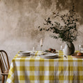 Large yellow gingham cotton tablecloth draped over a dining table, creating a fresh and timeless country-inspired setting.