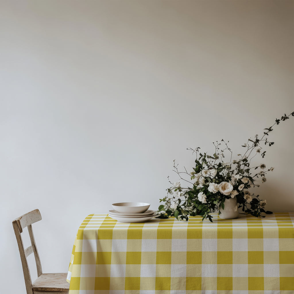 Yellow and white gingham cotton twill tablecloth styled on a dining table with white ceramic plates and a floral arrangement.