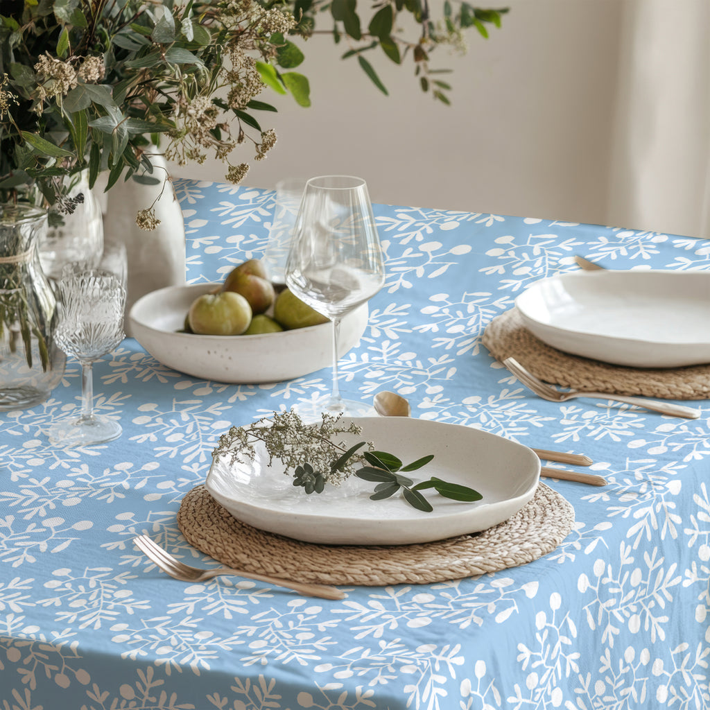 Light blue cotton twill tablecloth with white olive branch design, placed on a dining table with rustic ceramic plates and wine glasses.