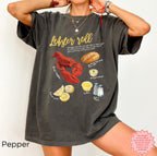 Unisex Comfort Colors 1717 t-shirt in Pepper grey featuring vibrant lobster roll graphic with lobster, bun, butter, mayonnaise, and lemon slices, perfect seafood lover shirt.