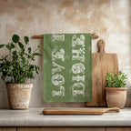 Decorative olive green tea towel styled with wooden utensils and herbs