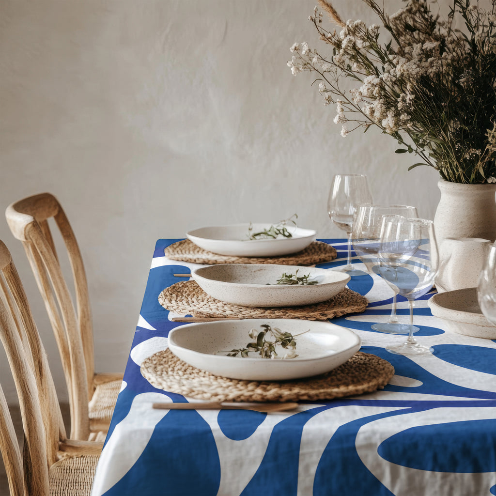 Blue abstract Mediterranean tablecloth displayed in a bright natural dining room with woven placemats