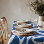 Blue abstract Mediterranean tablecloth displayed in a bright natural dining room with woven placemats