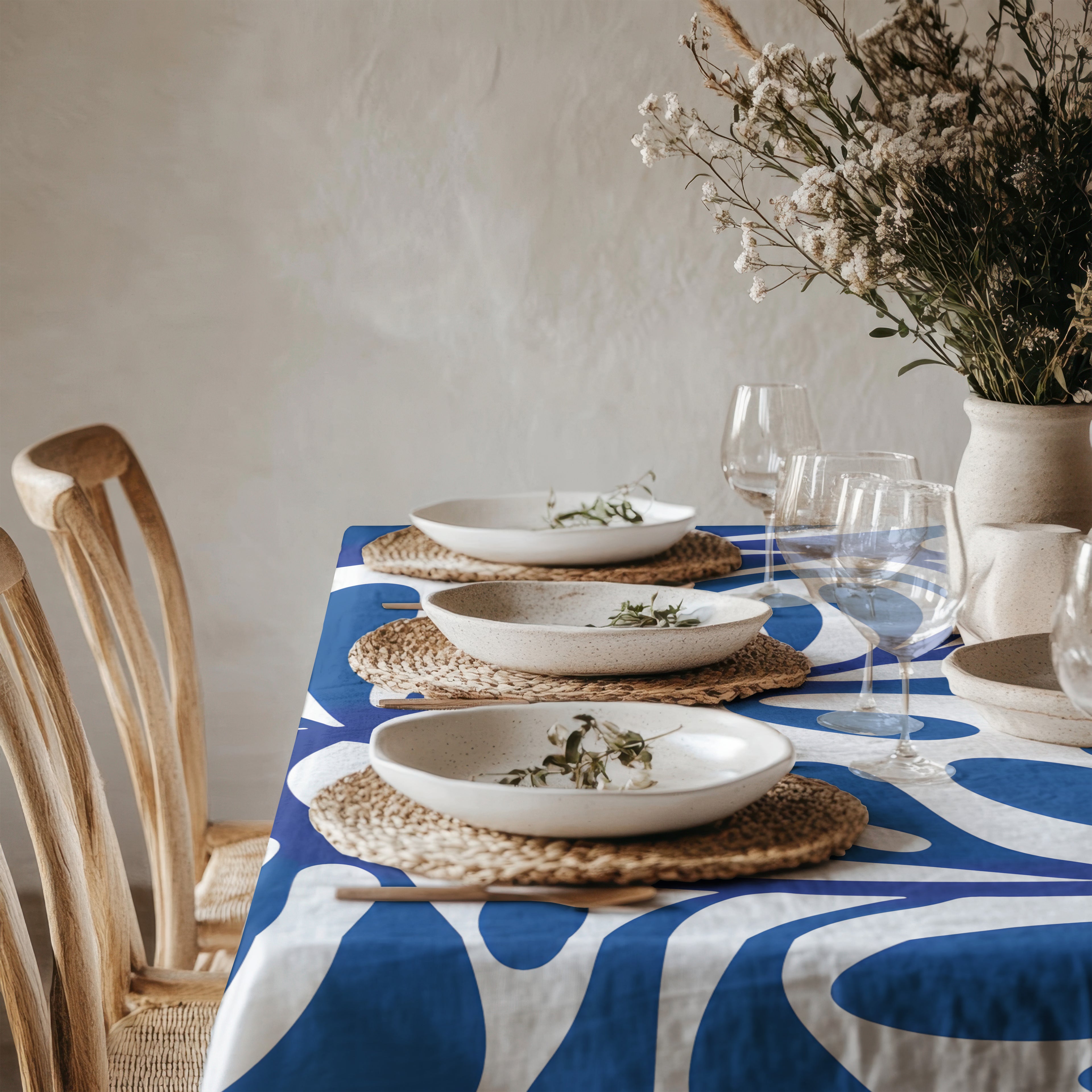 Blue abstract Mediterranean tablecloth displayed in a bright natural dining room with woven placemats