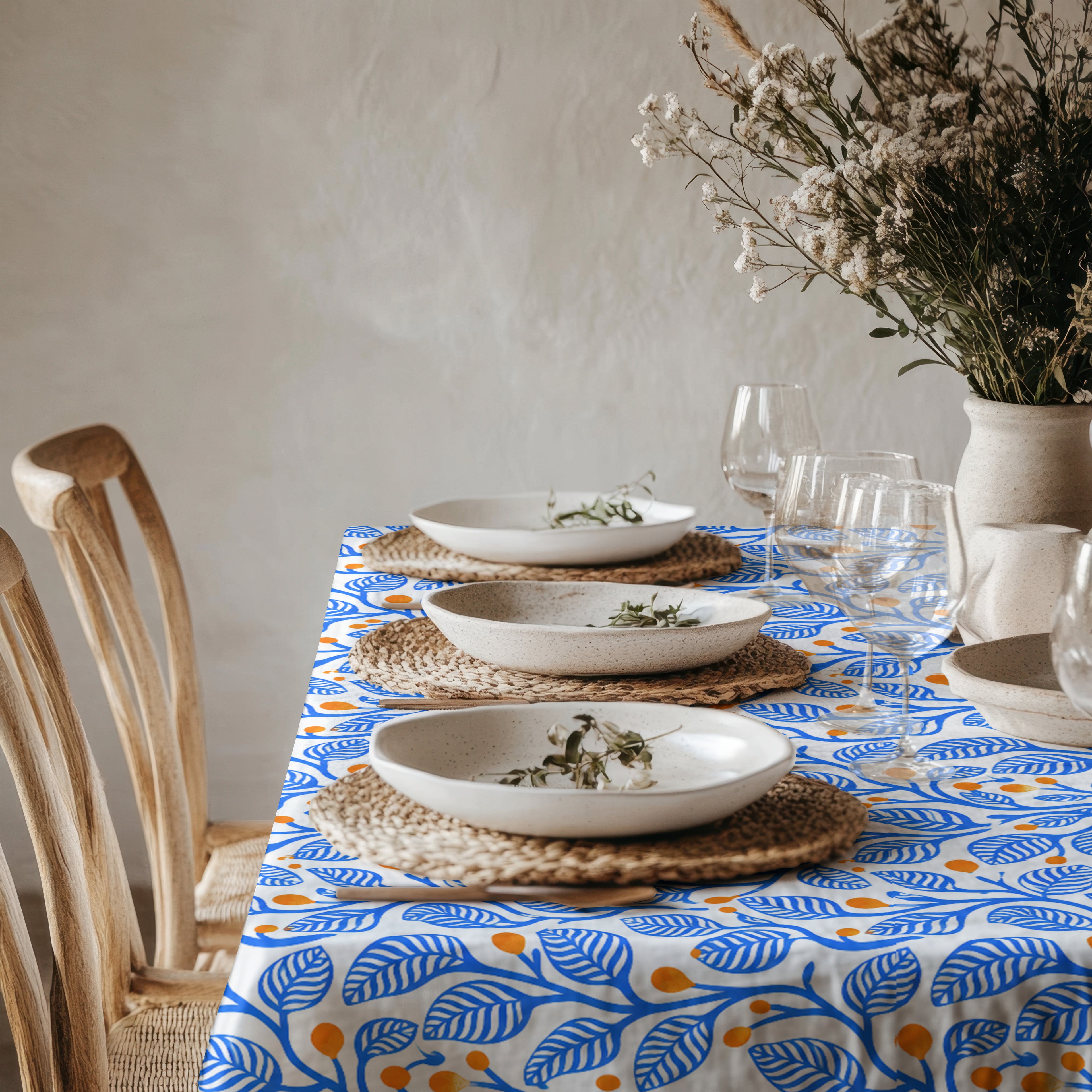 Mediterranean-inspired cotton twill tablecloth featuring hand-illustrated blue botanical branches and warm terracotta details.