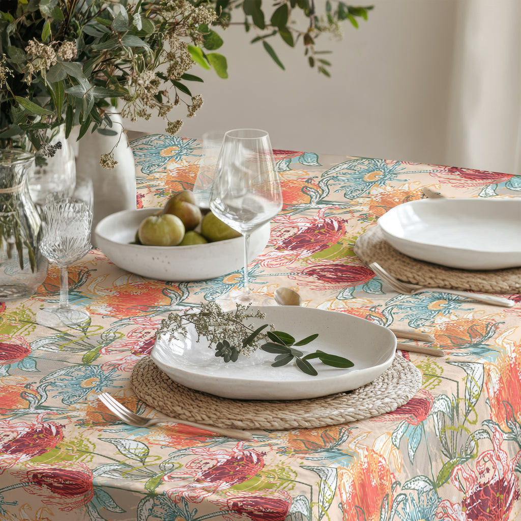 Close-up of colorful botanical tablecloth pattern with ceramic plates, woven placemats, and clear wine glasses