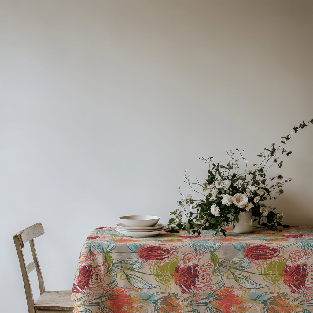 Mediterranean floral tablecloth with layered ceramic plates, greenery, and tall candles on a light-filled dining table