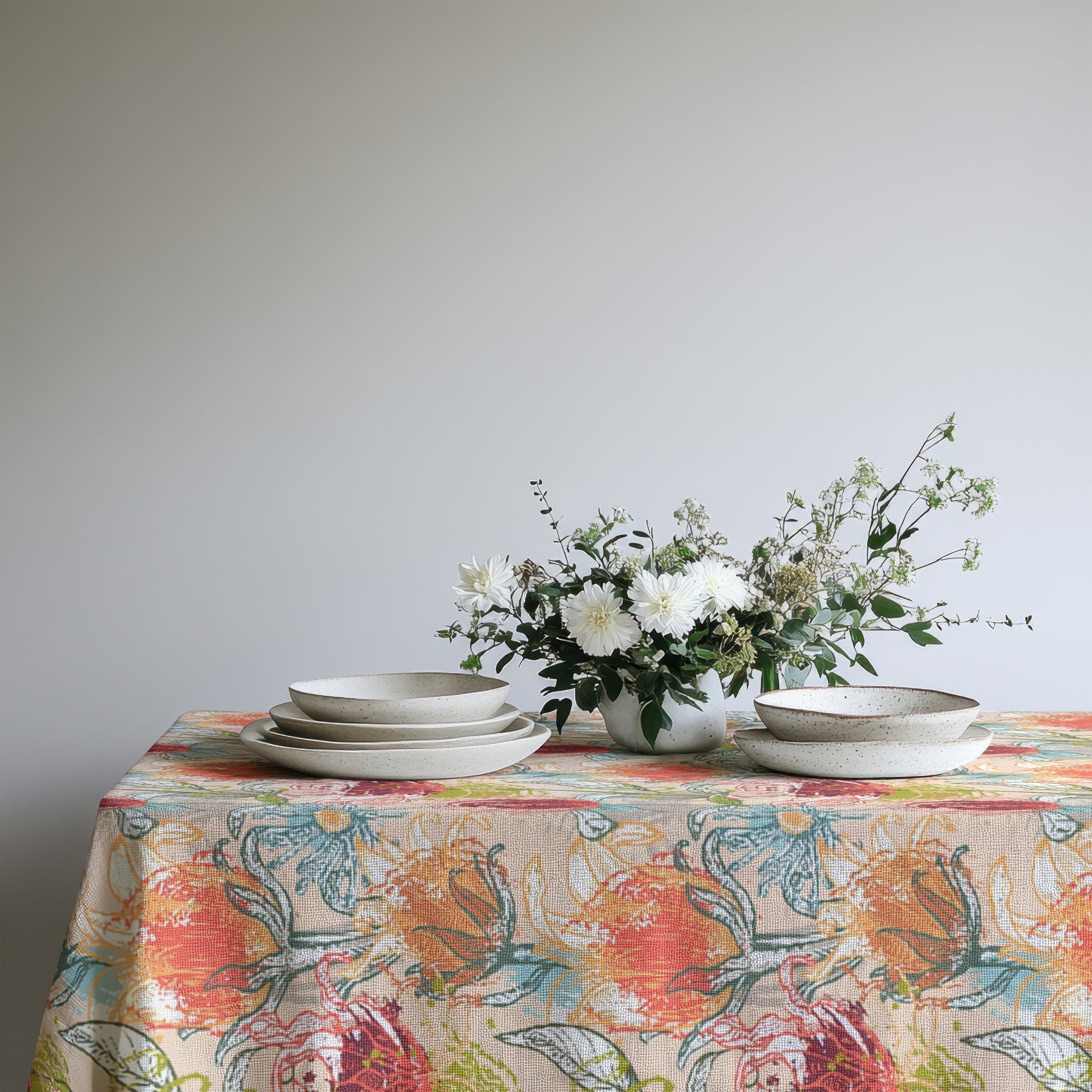 Modern Mediterranean floral tablecloth draped over dining table with simple place settings and fresh greenery