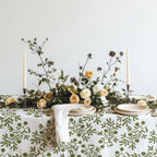Hand-drawn olive pattern cotton tablecloth featuring green botanical motifs on a white background, styled for elegant Mediterranean entertaining.