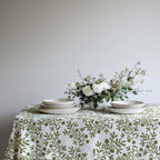 Modern Mediterranean dining table styled with an olive branch tablecloth, woven placemats, ceramic plates, and natural floral arrangements.
