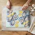 Watercolor oysters and lemons glass cutting board featuring coastal kitchen artwork on textured tempered glass