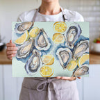 Coastal-inspired glass cutting board with hand-painted style oysters, lemons and soft seaside watercolor tones
