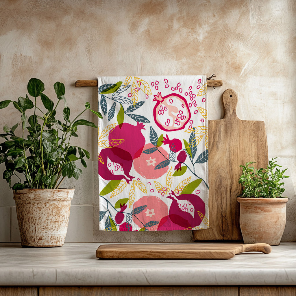Painted pomegranate tea towel hanging in a bright Mediterranean kitchen with wooden utensils and greenery