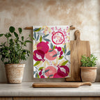 Painted pomegranate tea towel hanging in a bright Mediterranean kitchen with wooden utensils and greenery