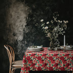 Mediterranean pomegranate tablecloth styled on a dining table in a dark moody interior with rustic chairs and ceramic tableware