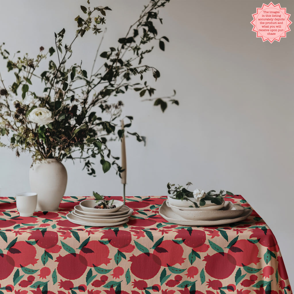 Pomegranate patterned tablecloth styled with ceramic dishes, fruit bowl, and wine glasses in a rustic Mediterranean dining setting