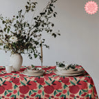 Pomegranate patterned tablecloth styled with ceramic dishes, fruit bowl, and wine glasses in a rustic Mediterranean dining setting