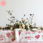 Italian food-themed red tablecloth with hand-drawn illustrations of pasta, ice cream, and pizza, placed on a table with a floral arrangement, plates, and candles.