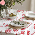 Summer-inspired red Italian food tablecloth with hand-drawn food illustrations, placed on a dining table with plates, glasses of wine, and a vase of flowers.