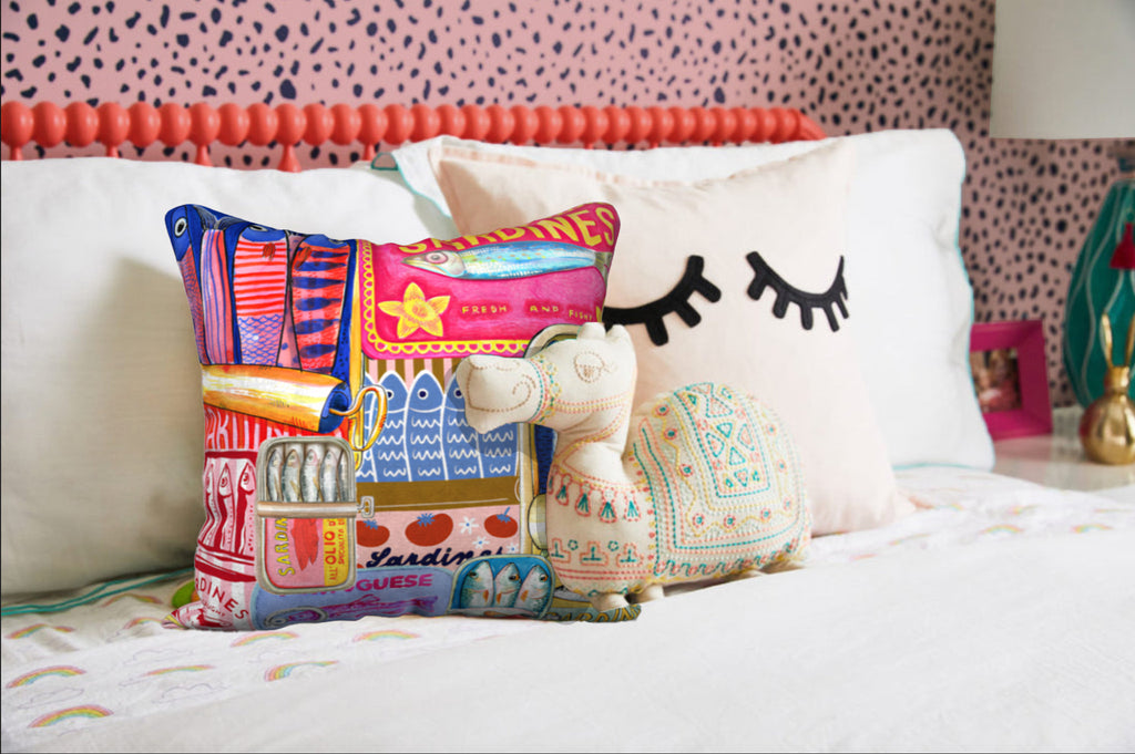 Sardines decorative cushion on a bed, showcasing the retro sardine can design in vibrant hues – available in 18x18 inches, with 4 fabric options.
