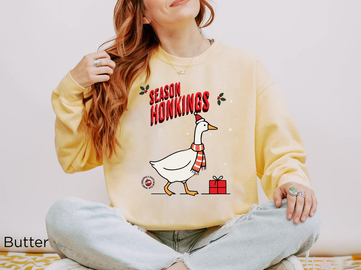 Funny Christmas goose sweatshirt in Butter with “Season Honkings” lettering and a festive present illustration.